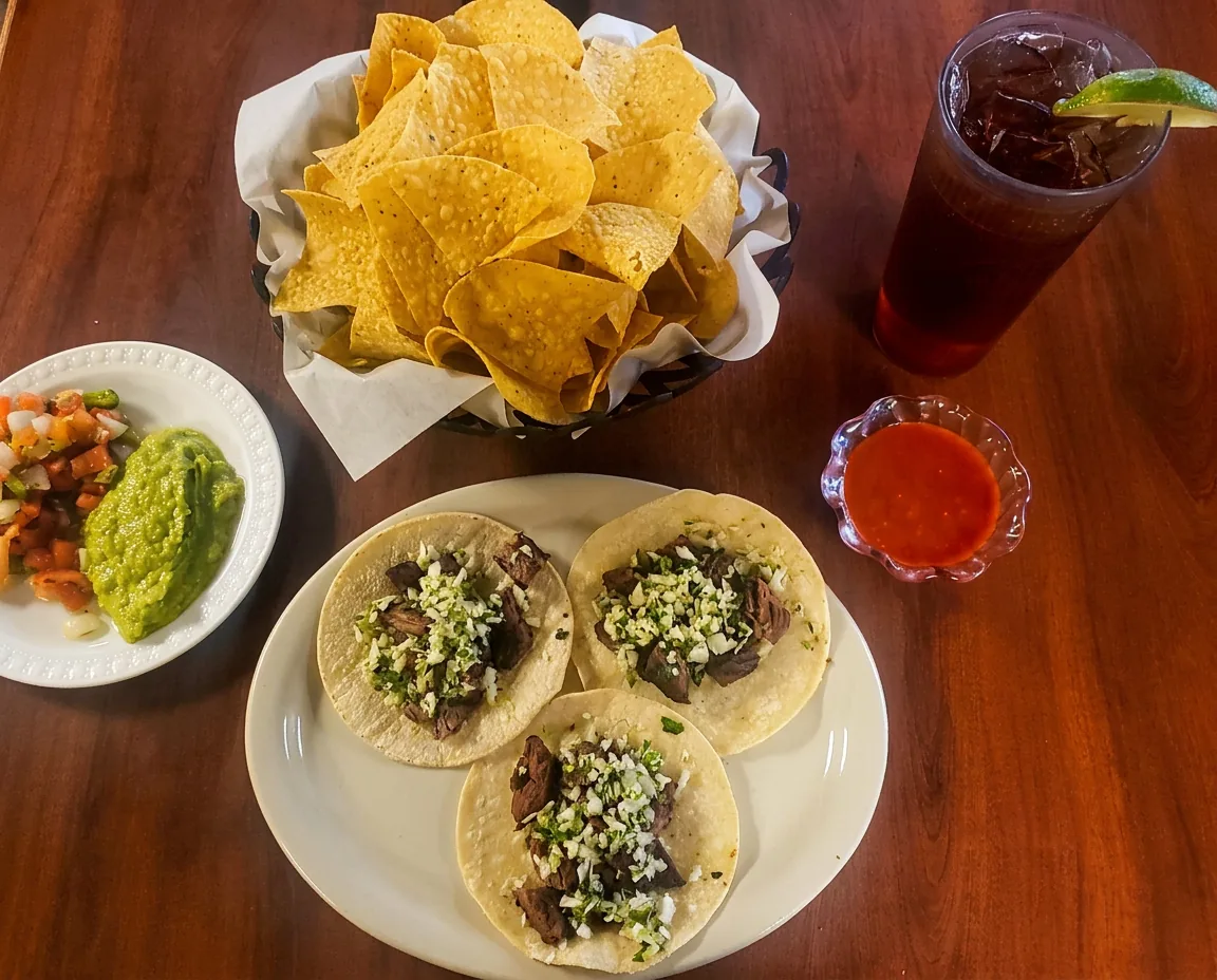 Street tacos, chips, guacamole, pico de gallo and hot sauce on a wooden table at Taco El Conquistador